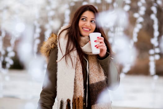 Portrait of young woman in a snow park drinks tea