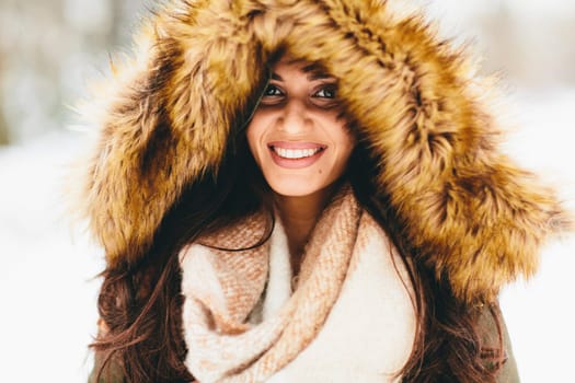 Young woman with a fur hood in the park on the snow