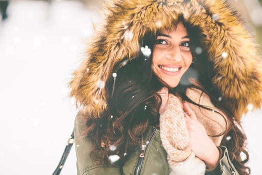 Young woman with a fur hood in the park on the snow
