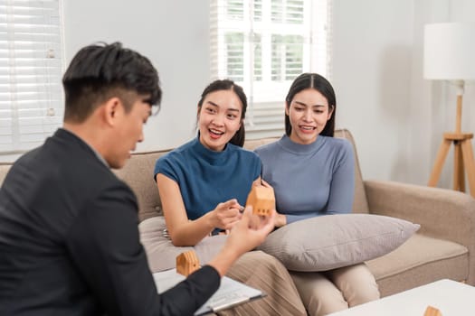 A real estate agent enthusiastically explains property features to two interested buyers in a welcoming living room.