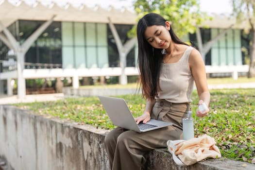 A young woman engages with her laptop in a park, showcasing her commitment to sustainability with eco-friendly choices nearby.