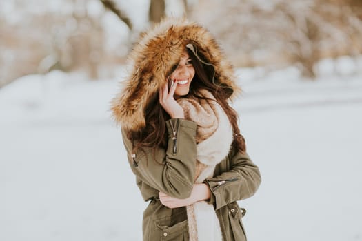 Smiling young woman using phone in park at cold winter day