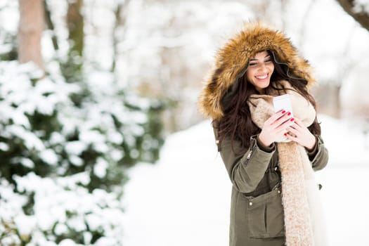 Smiling young woman using phone in park at cold winter day
