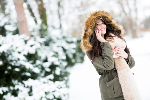 Smiling young woman using phone in park at cold winter day
