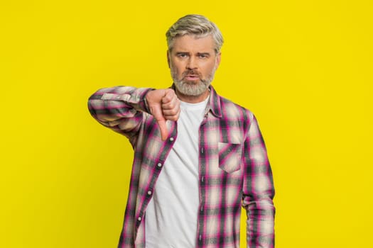 Dislike. Upset unhappy Caucasian man showing thumbs down sign gesture, expressing discontent, disapproval, dissatisfied negative feedback. Handsome mature guy indoors isolated on yellow background
