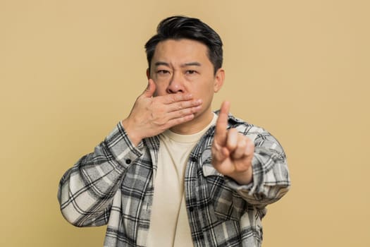 I will not say anything. Strict Asian middle-aged man closing mouth with hands, looking intimidated scared at camera gestures no refusing to tell terrible secret unbelievable truth. Mature Chinese guy