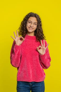 Okay. Happy Caucasian young teenager girl looking approvingly at camera showing ok gesture, like sign positive feedback, approve something good, celebrate victory. Teen child kid on yellow background