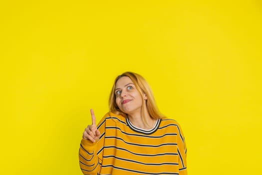 Good idea. Inspired young blonde woman pointing finger up with open mouth having plan, startup, showing inspiration motivation Eureka gesture problem solution. Girl isolated on yellow background