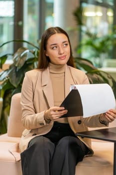 Caucasian young businesswoman working with documents, analyzing information, reading papers prepare financial report. Young female entrepreneur in formal analyzing graph documents in office lobby.