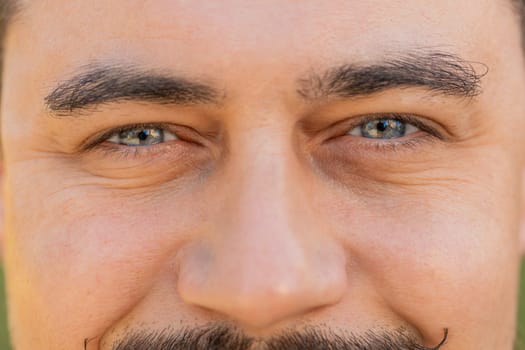 Closeup macro portrait of natural mature handsome man's eyes, smiling looking at camera. Attractive gray eyes of man face, adult guy male model. Caucasian tourist against blur background. Lifestyles.