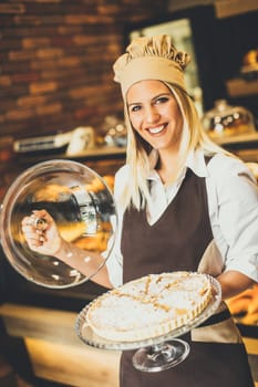 Bakery female worker posing with apple tart in baker shop