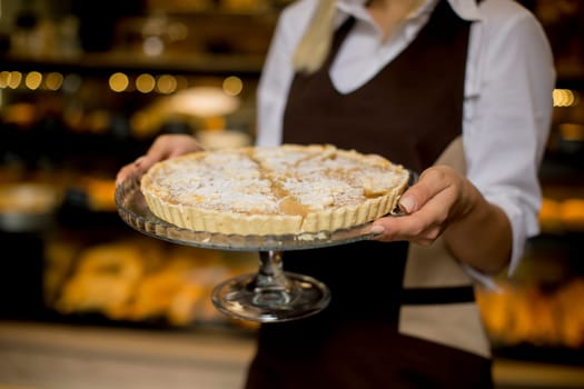 Portrait of female bakery worker posing with apple tart in baker shop