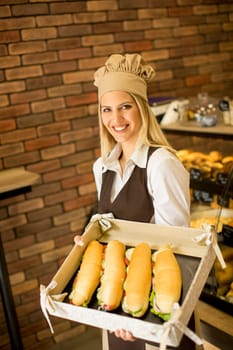 Portrait of female baker posing with various types of sandwiches in the baker shop