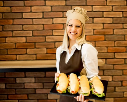Beautiful female bakery posing with various types of sandwiches in the bakery shop