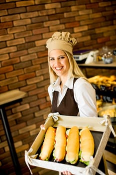 Beautiful female bakery posing with various types of sandwiches in the baker shop