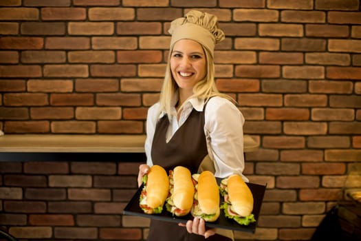 Portrait of female baker posing with various types of sandwiches in the baker shop