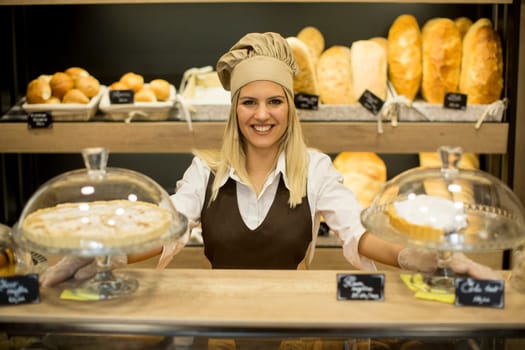 Portrait of friendly female baker with fresh bread smiling in bakery