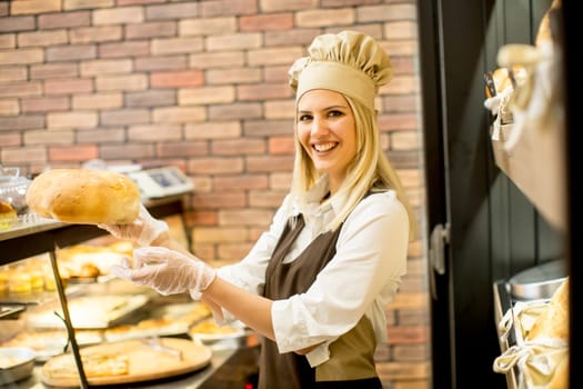 Young woman takes fresh bread from the shelves in a baker shop