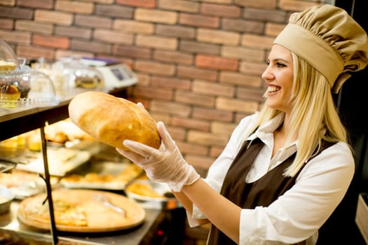 Young woman takes fresh bread from the shelves in a baker shop