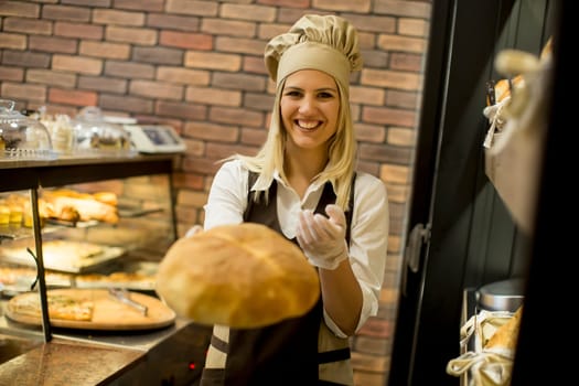 Pretty young woman selling soft  fresh bread in the bakery
