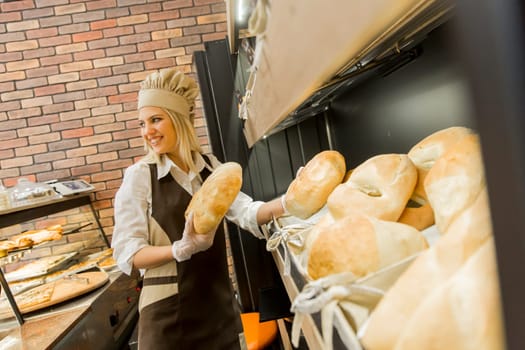 Young woman takes fresh bread from the shelves in a baker shop