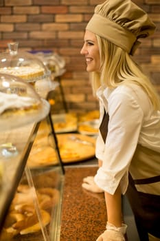 Pretty young woman with a cap selling fresh products in the bakery
