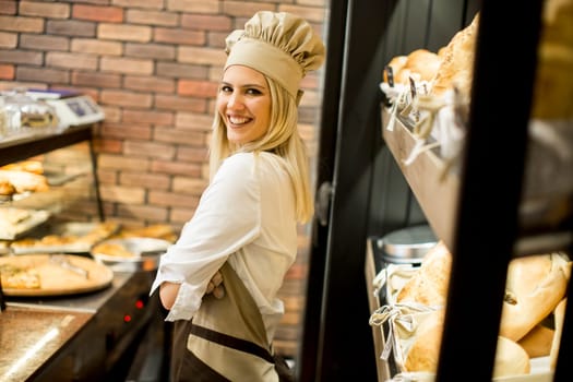 Young woman posing in front of shelves in  baker shop and smiling