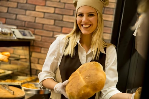 Pretty young woman selling soft  fresh bread in the bakery