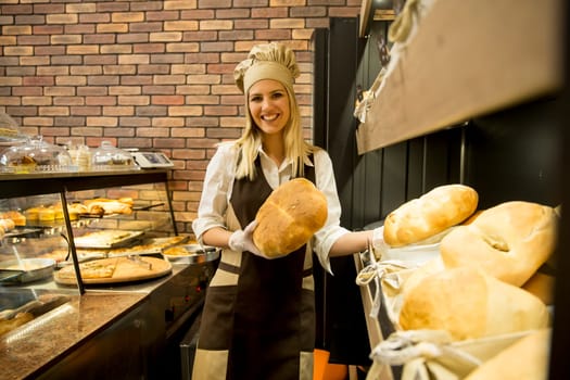 Pretty young woman selling soft  fresh bread in the bakery