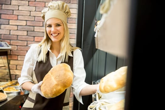 Young woman takes fresh bread from the shelves in a baker shop