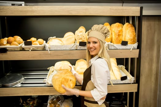 Pretty young woman selling soft  fresh bread in the bakery