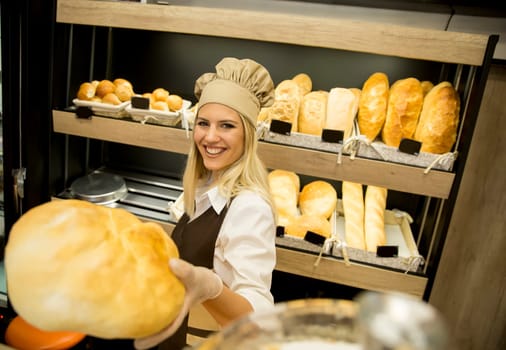 Pretty young woman selling soft  fresh bread in the bakery