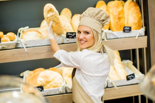 Young woman takes fresh bread from the shelves in a baker shop