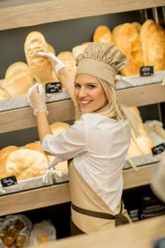 Pretty young woman selling fresh bread in the bakery