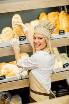 Young woman takes fresh bread from the shelves in a baker shop