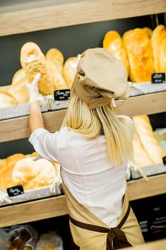 Young woman takes fresh bread from the shelves in a baker shop