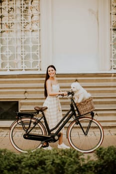 Pretty young woman with white bichon frise dog in the basket of electric bike