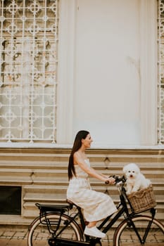 Pretty young woman with white bichon frise dog in the basket of electric bike