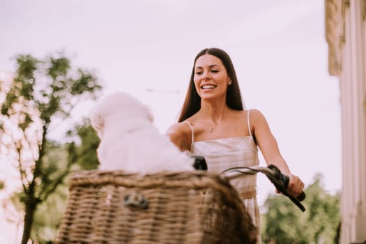 Pretty young woman with white bichon frise dog in the basket of electric bike