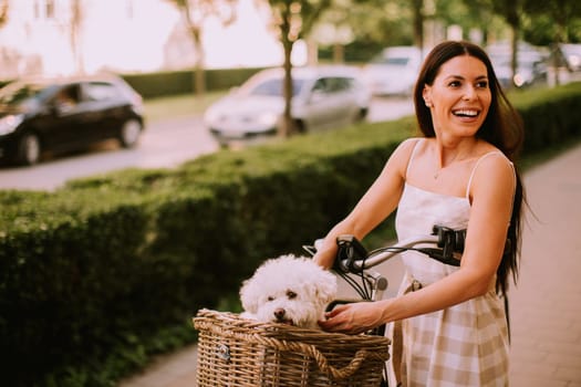 Pretty young woman with white bichon frise dog in the basket of electric bike