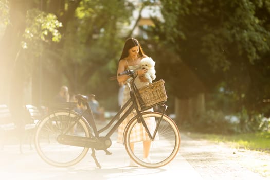 Pretty young woman with white bichon frise dog in the basket of electric bike