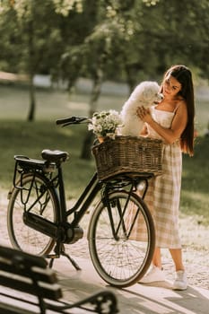 Pretty young woman with white bichon frise dog in the basket of electric bike