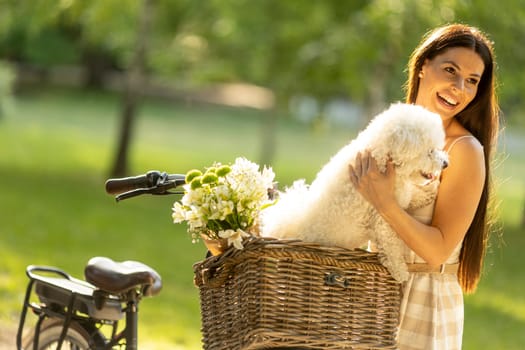 Pretty young woman with white bichon frise dog in the basket of electric bike