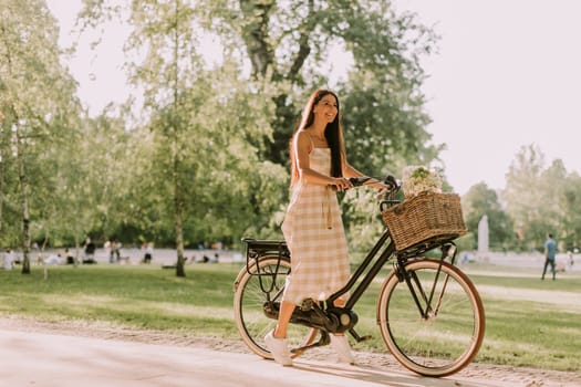 Pretty young woman with electric bike and flowers in the basket