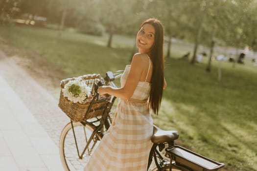Pretty young woman with flowers in the basket of electric bike
