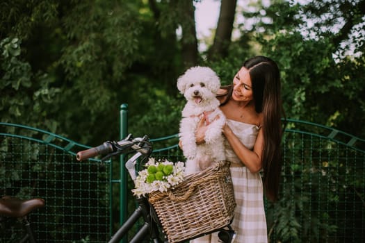 Pretty young woman with white bichon frise dog in the basket of electric bike