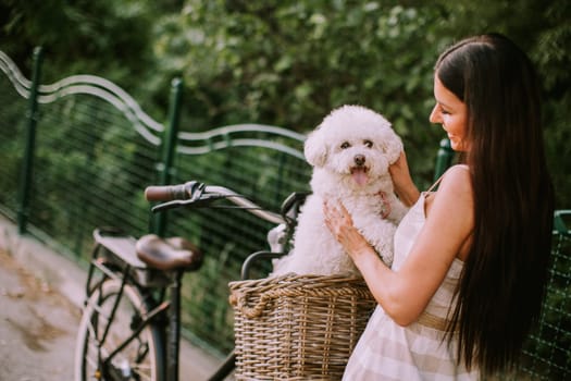 Pretty young woman with white bichon frise dog in the basket of electric bike