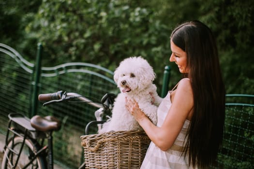 Pretty young woman with white bichon frise dog in the basket of electric bike