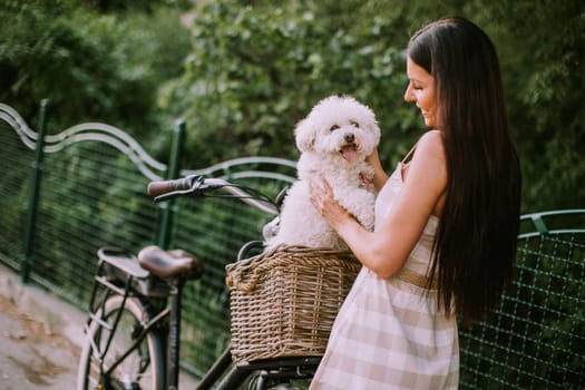 Pretty young woman with white bichon frise dog in the basket of electric bike