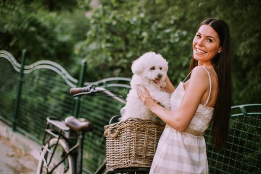 Pretty young woman with white bichon frise dog in the basket of electric bike